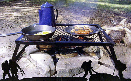 Camp cookware on a fire grate with frying pans and coffee pot